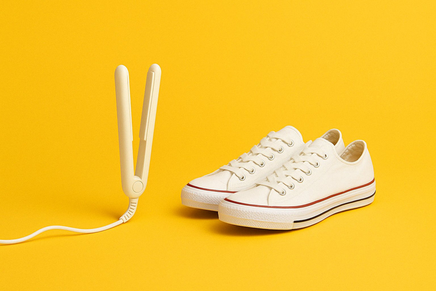 White hair straightener and white canvas sneakers with red accents, neatly positioned on a vibrant yellow background, symbolizing trending and popular products.